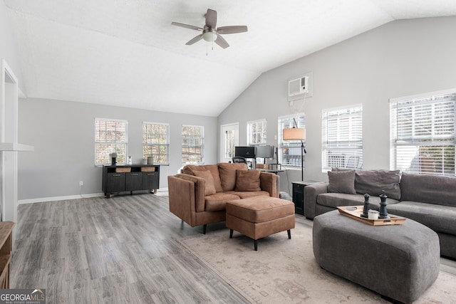 living room featuring baseboards, a ceiling fan, light wood-style flooring, an AC wall unit, and high vaulted ceiling