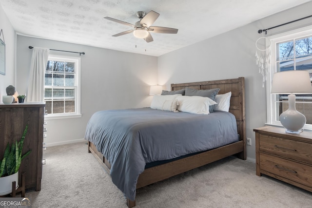 bedroom featuring multiple windows, a textured ceiling, light colored carpet, and ceiling fan