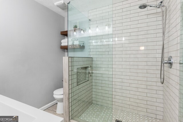 bathroom featuring a textured ceiling, a stall shower, toilet, and baseboards