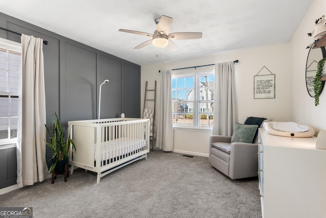 bedroom featuring visible vents, light carpet, ceiling fan, a nursery area, and baseboards