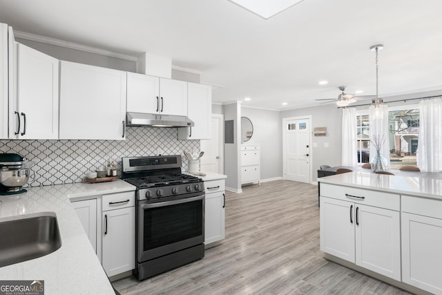 kitchen featuring white cabinets, crown molding, under cabinet range hood, and gas range