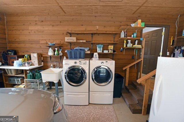 clothes washing area featuring sink, washer and dryer, and wood walls