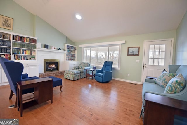 living room with plenty of natural light, a brick fireplace, high vaulted ceiling, and light hardwood / wood-style flooring