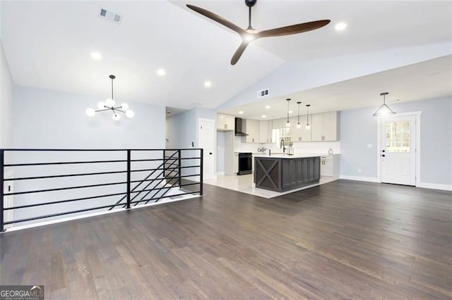 unfurnished living room with ceiling fan with notable chandelier, dark wood-type flooring, and vaulted ceiling