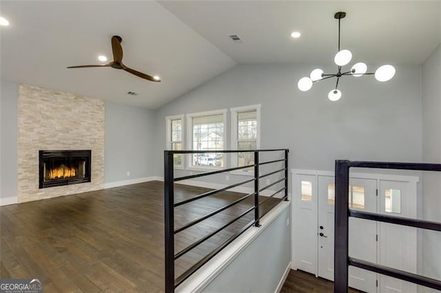 interior space featuring dark hardwood / wood-style flooring, a stone fireplace, vaulted ceiling, and ceiling fan with notable chandelier