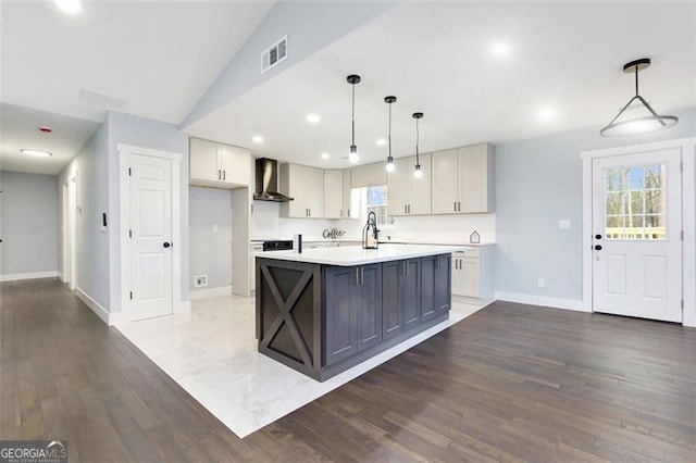 kitchen with an island with sink, dark hardwood / wood-style floors, wall chimney range hood, and decorative light fixtures