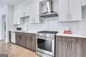 kitchen with white cabinetry, sink, white dishwasher, gas range, and wall chimney range hood