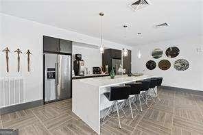 kitchen with hanging light fixtures, an island with sink, a breakfast bar, and stainless steel fridge