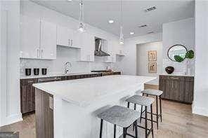 kitchen with decorative light fixtures, a kitchen island, white cabinets, light hardwood / wood-style floors, and wall chimney range hood