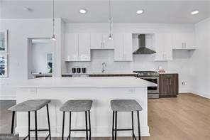 kitchen with pendant lighting, stainless steel stove, white cabinetry, a spacious island, and wall chimney exhaust hood