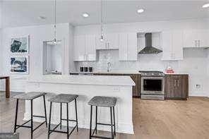 kitchen with hanging light fixtures, white cabinetry, stainless steel range, and wall chimney exhaust hood