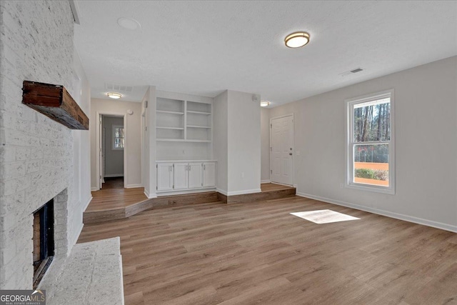 unfurnished living room featuring a brick fireplace, a textured ceiling, light hardwood / wood-style floors, and a healthy amount of sunlight