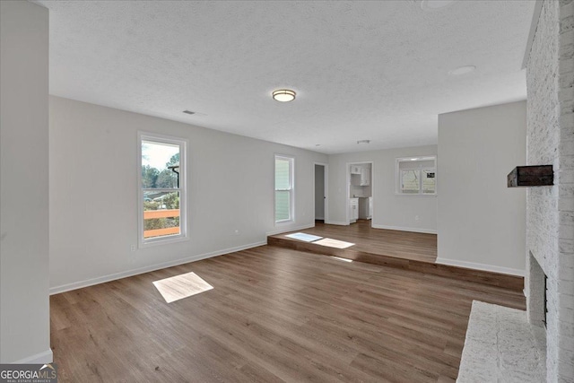 unfurnished living room featuring a brick fireplace, hardwood / wood-style floors, and a textured ceiling