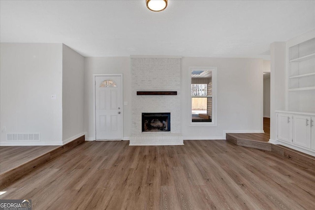 unfurnished living room with a brick fireplace, built in features, and light wood-type flooring