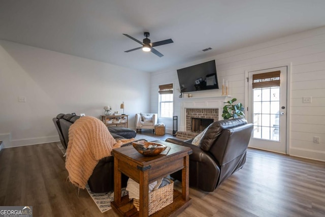 living room with ceiling fan, hardwood / wood-style floors, and a brick fireplace