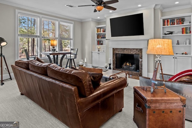 carpeted living room featuring built in shelves, ornamental molding, a high end fireplace, and ceiling fan