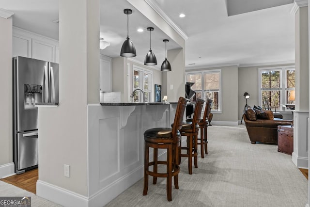 kitchen with pendant lighting, white cabinets, crown molding, stainless steel refrigerator with ice dispenser, and light stone countertops