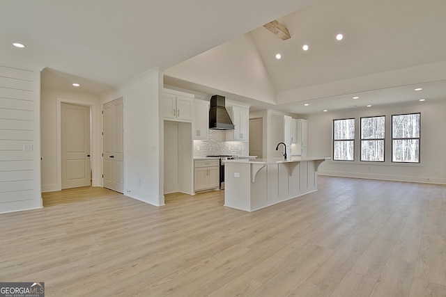 kitchen with custom exhaust hood, a center island with sink, white cabinets, and light hardwood / wood-style floors