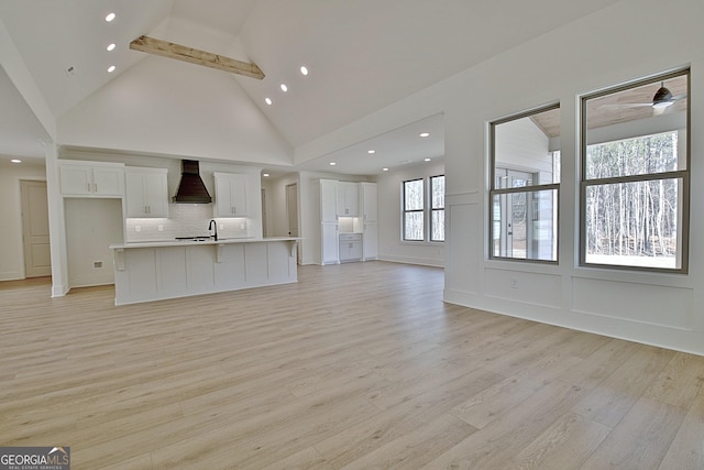 unfurnished living room featuring sink, light hardwood / wood-style flooring, ceiling fan, beam ceiling, and high vaulted ceiling