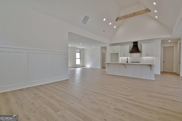 kitchen with a large island with sink, white cabinetry, custom range hood, and light wood-type flooring