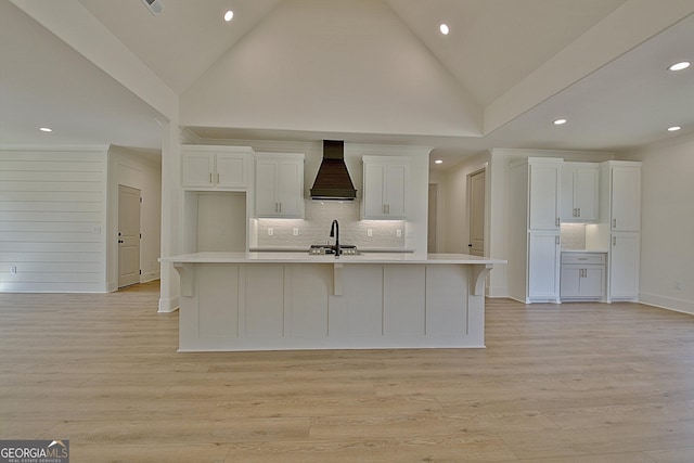 kitchen featuring light wood-type flooring, custom exhaust hood, white cabinets, and a center island with sink