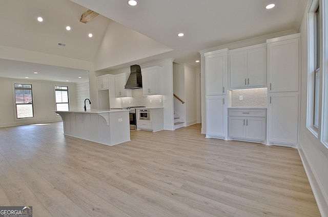 kitchen featuring premium range hood, white cabinetry, stainless steel range, light hardwood / wood-style floors, and an island with sink