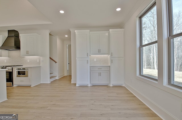 kitchen with premium range hood, white cabinetry, backsplash, stainless steel appliances, and light wood-type flooring