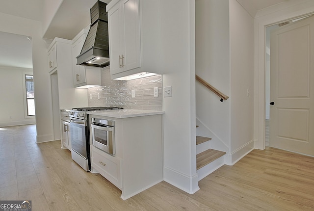 kitchen with tasteful backsplash, gas range, white cabinets, and light hardwood / wood-style flooring