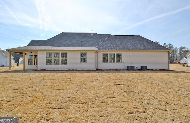 rear view of property with central AC unit and a lawn