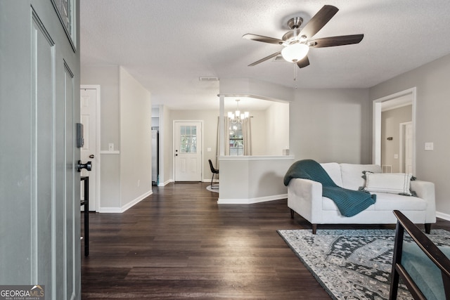 living room featuring dark hardwood / wood-style flooring, ceiling fan with notable chandelier, and a textured ceiling