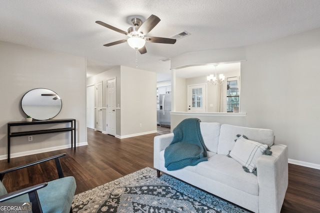 living room featuring dark hardwood / wood-style floors, ceiling fan with notable chandelier, and a textured ceiling