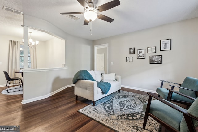 living area featuring ceiling fan with notable chandelier, a textured ceiling, and dark hardwood / wood-style flooring