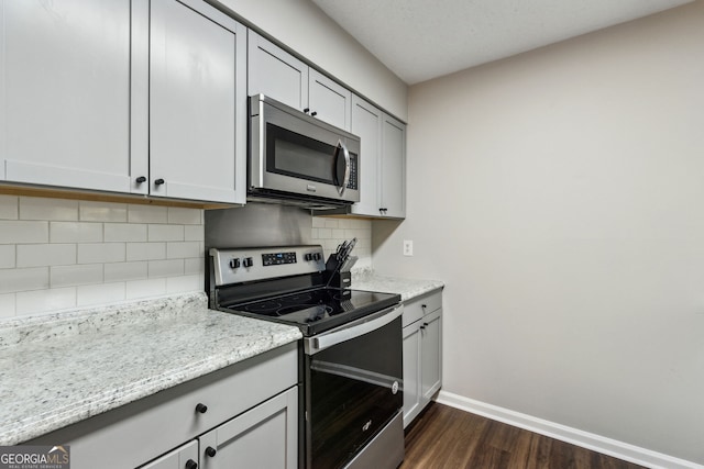 kitchen with dark wood-type flooring, stainless steel appliances, light stone countertops, and backsplash