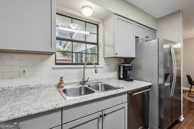 kitchen featuring sink, appliances with stainless steel finishes, dark hardwood / wood-style flooring, light stone countertops, and decorative backsplash