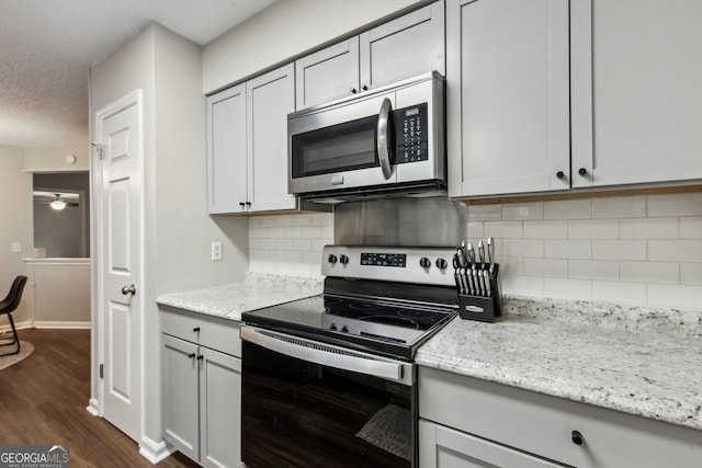 kitchen featuring dark hardwood / wood-style floors, backsplash, stainless steel appliances, light stone countertops, and a textured ceiling