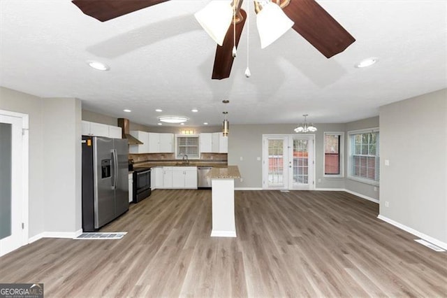 kitchen with wall chimney range hood, sink, hanging light fixtures, stainless steel appliances, and white cabinets