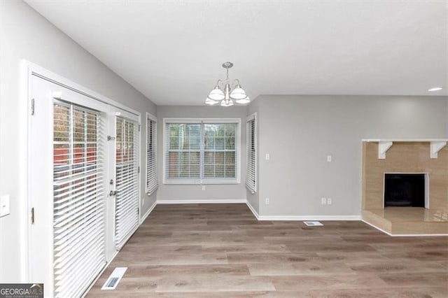 unfurnished dining area featuring wood-type flooring, a chandelier, and a tile fireplace