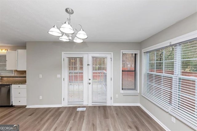 unfurnished dining area featuring french doors, light hardwood / wood-style floors, and a notable chandelier