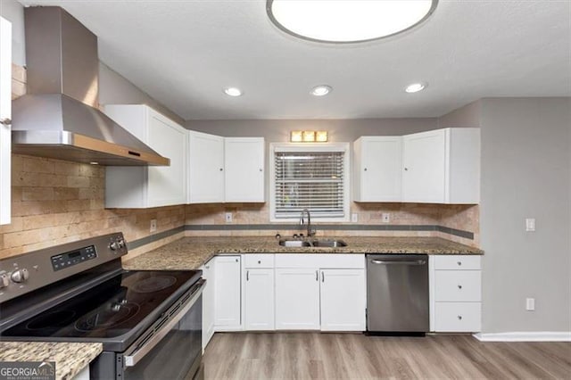 kitchen featuring sink, white cabinetry, dark stone countertops, stainless steel appliances, and wall chimney exhaust hood