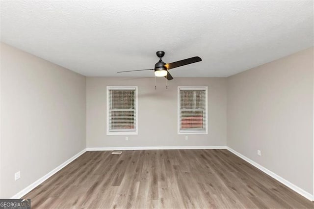 empty room with ceiling fan, wood-type flooring, and a textured ceiling