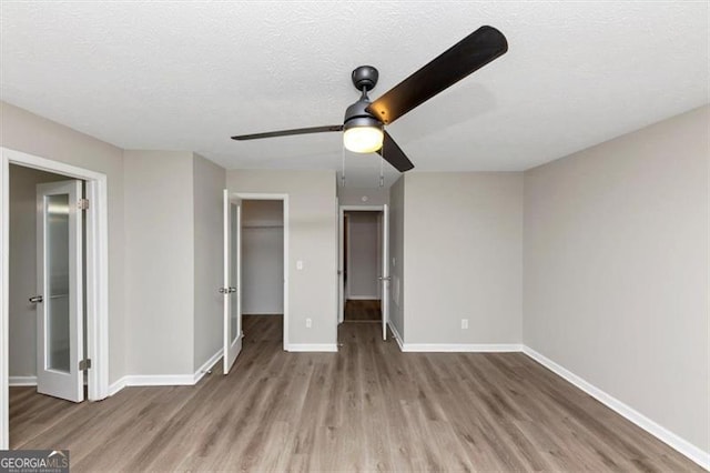 unfurnished bedroom featuring hardwood / wood-style flooring, ceiling fan, a spacious closet, and a textured ceiling