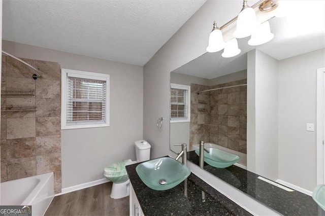 full bathroom featuring hardwood / wood-style flooring, vanity, tiled shower / bath combo, toilet, and a textured ceiling