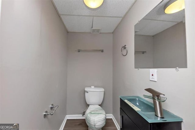 bathroom with vanity, wood-type flooring, toilet, and a drop ceiling