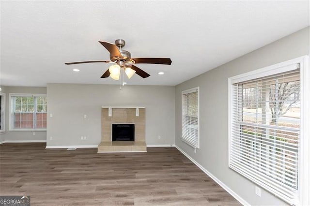 unfurnished living room featuring a tiled fireplace, hardwood / wood-style floors, and ceiling fan