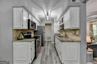 kitchen with white cabinetry, sink, light stone counters, light hardwood / wood-style floors, and stainless steel appliances