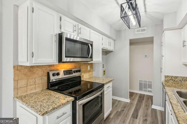 kitchen featuring pendant lighting, backsplash, white cabinets, stainless steel appliances, and light wood-type flooring