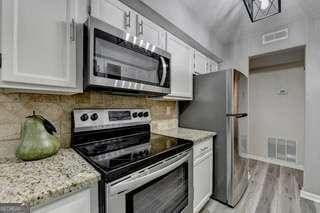 kitchen featuring stainless steel appliances, white cabinetry, light stone countertops, and backsplash