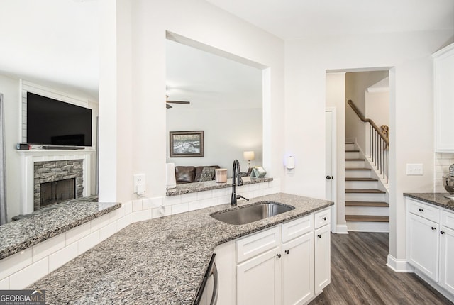 kitchen with a stone fireplace, sink, white cabinets, dark stone counters, and dark wood-type flooring