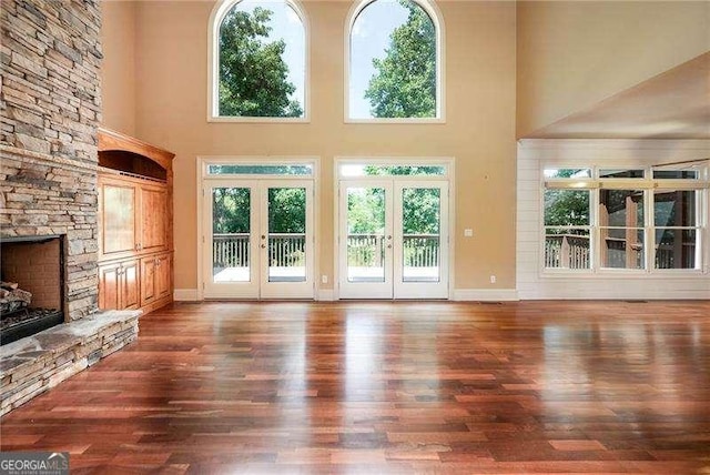 unfurnished living room featuring a stone fireplace, a wealth of natural light, dark hardwood / wood-style flooring, and french doors