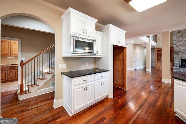 kitchen featuring white cabinetry, dark stone countertops, dark hardwood / wood-style floors, stainless steel microwave, and a stone fireplace